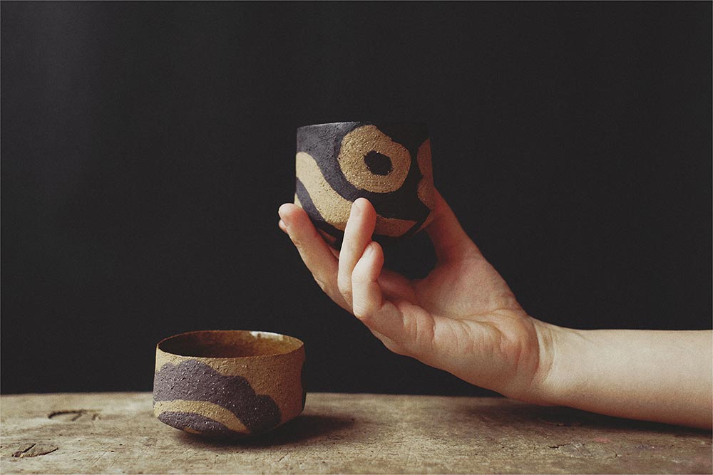 Hand hält kleinen braunen Keramikbecher – Atelier Tonga.