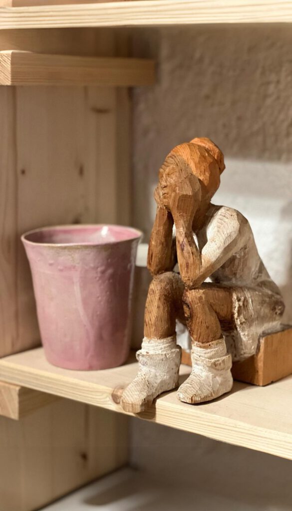 Holzfigur neben rosa Keramikbecher auf Regalbrett im Atelier Tonga.