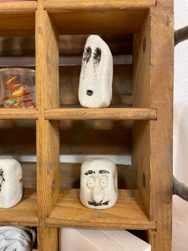 Keramikmasken mit Gesichtern im Holzregal – Atelier Tonga.