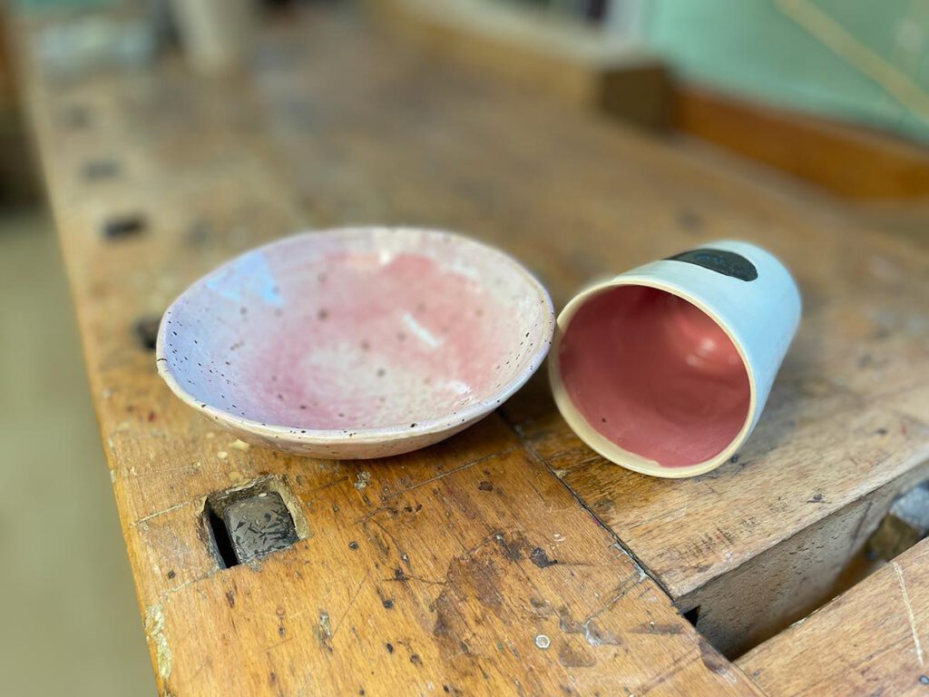 handgefertigter Keramikbecher und kleine Schüssel in Rosa und Weiß auf alter Werkbank – Atelier Tonga München.