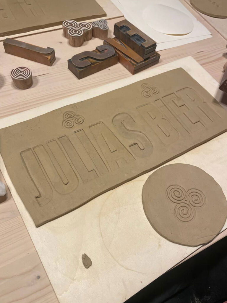 Handgefertigte Tonplatte mit Schriftprägung ‚Julias Bier‘ und dekorativen Spiralen, gestaltet mit Keramikstempeln im Atelier.