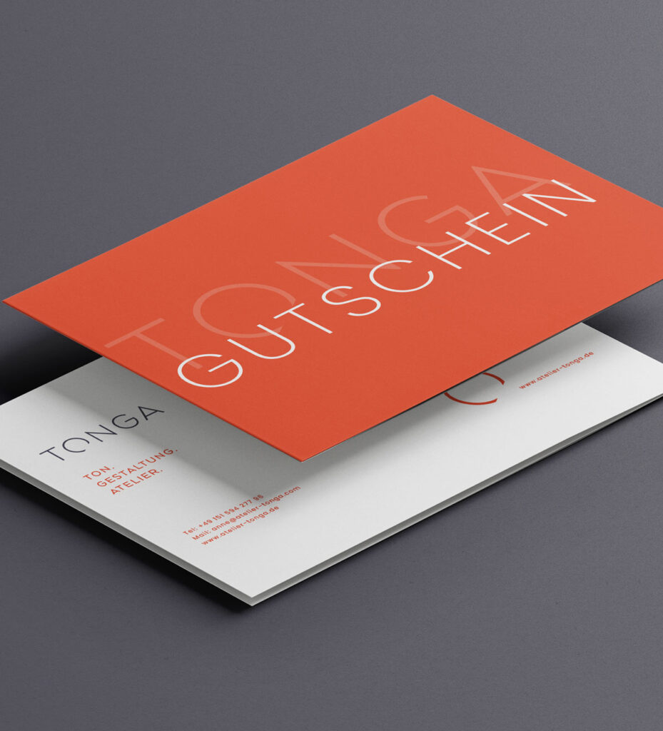 Minimalistischer Geschenkgutschein des Atelier Tonga: eine rote Karte mit dem weißen Schriftzug ‚GUTSCHEIN‘ und dem dezenten Hintergrundtext ‚TONGA‘ liegt auf einer hellen Karte mit Kontaktdaten des Ateliers. Elegantes, modernes Design auf dunklem Untergrund.
